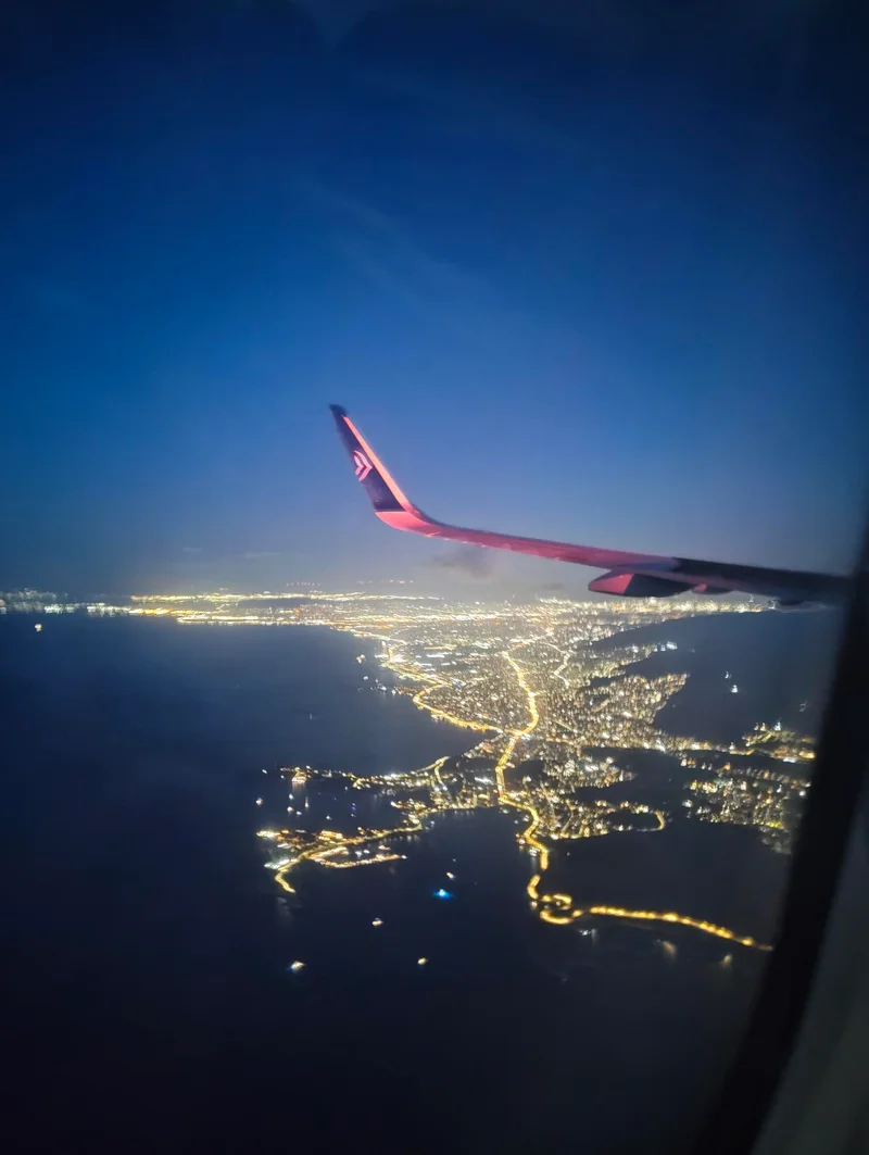 Blick aus einem Flugzeug auf einen beleuchteten Küstenort bei Nacht